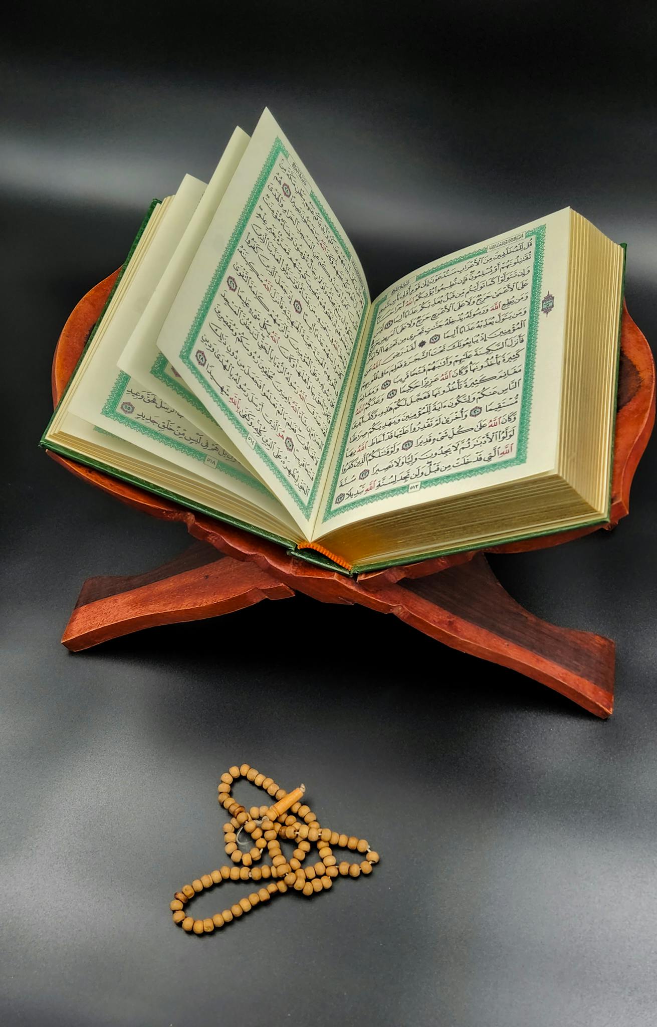 An open Quran resting on a wooden stand with prayer beads placed beside it, emphasizing spirituality and study.